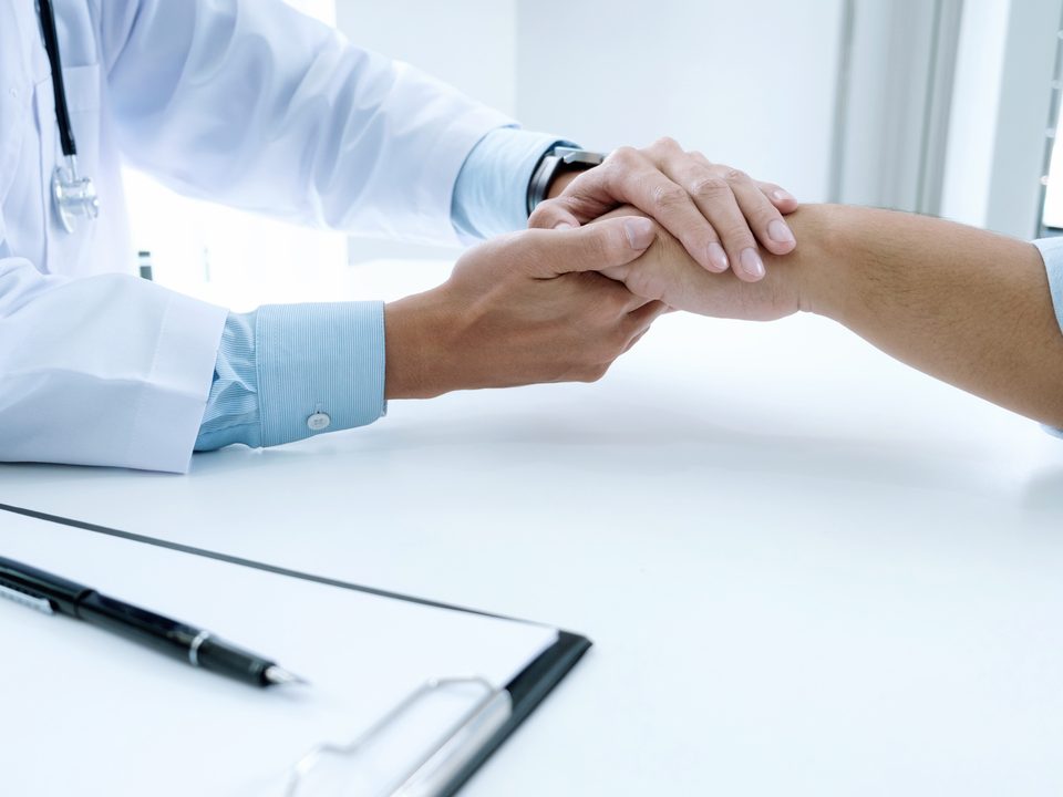 Diagnóstico precoce: médico aperta mão de paciente em gesto de apoio.