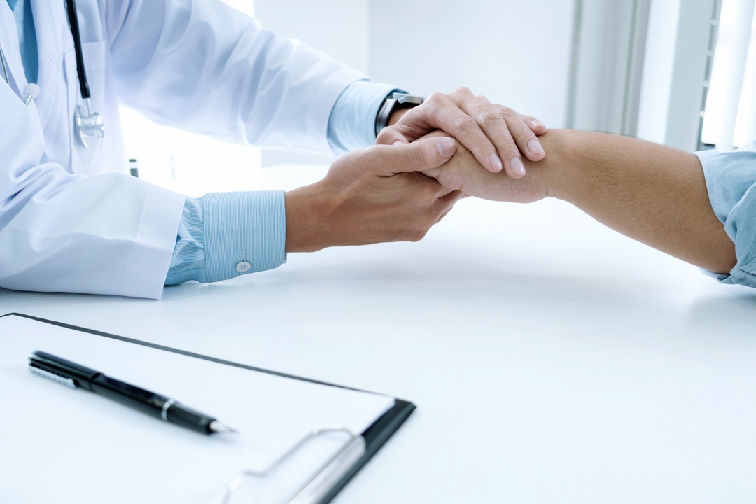 Diagnóstico precoce: médico aperta mão de paciente em gesto de apoio.