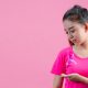 Autoexame de mama: Mulher apalpando mama enquanto usa camiseta rosa
