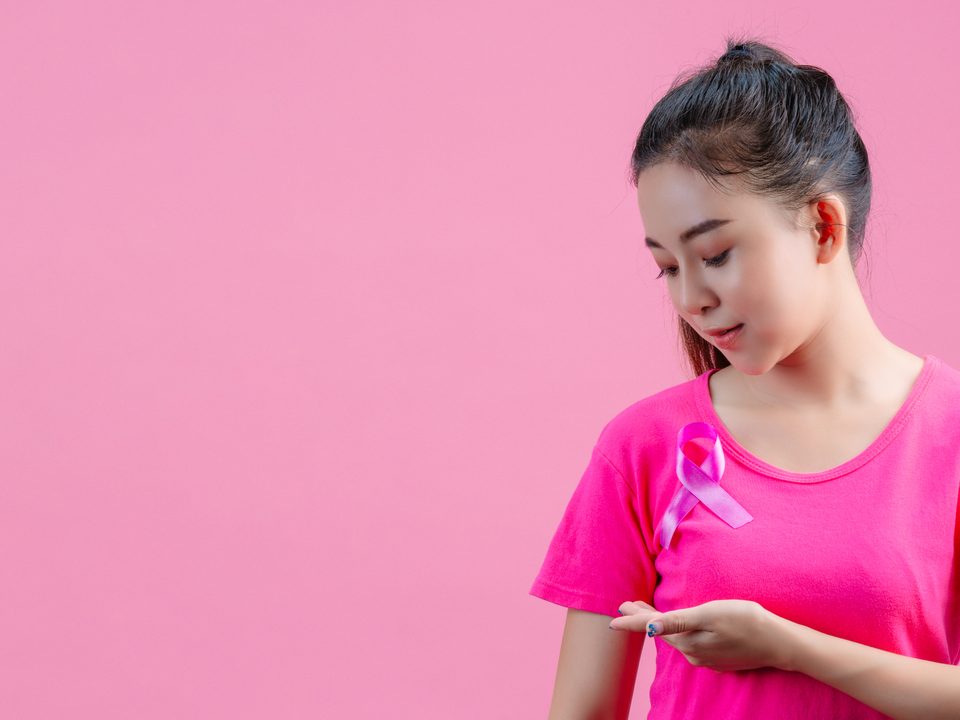 Autoexame de mama: Mulher apalpando mama enquanto usa camiseta rosa