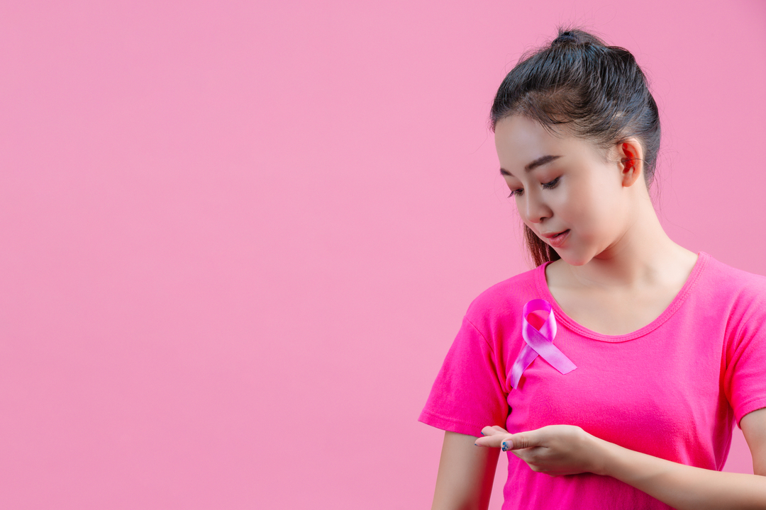 Autoexame de mama: Mulher apalpando mama enquanto usa camiseta rosa