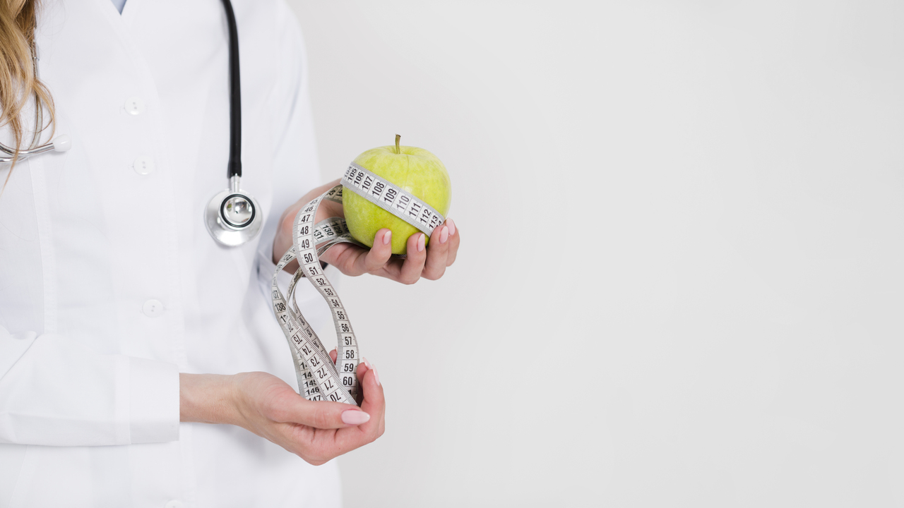 Jejum para exames: médica segurando maçã e fita métrica